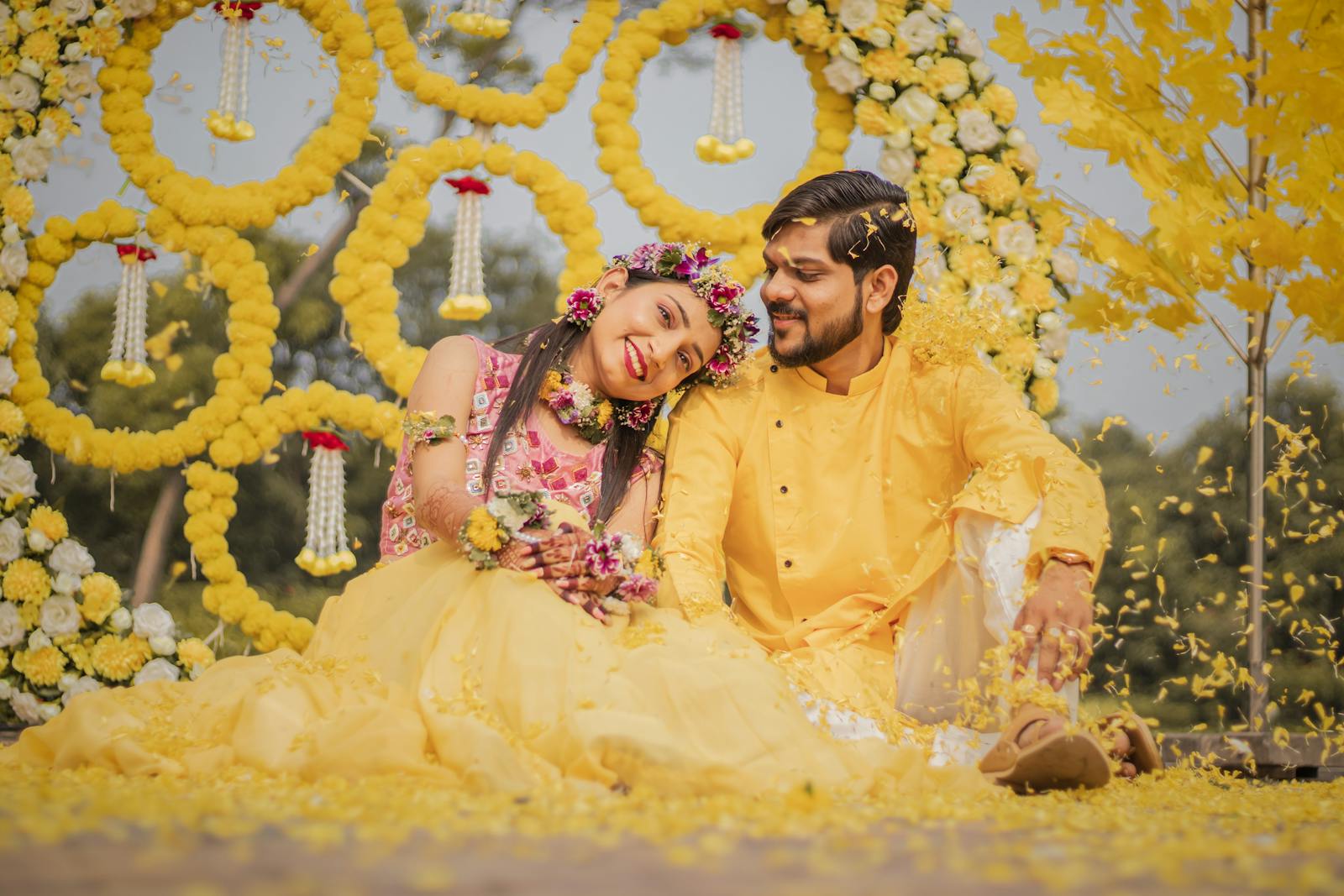 Vibrant Indian couple enjoying a traditional Haldi ceremony with yellow floral decor.